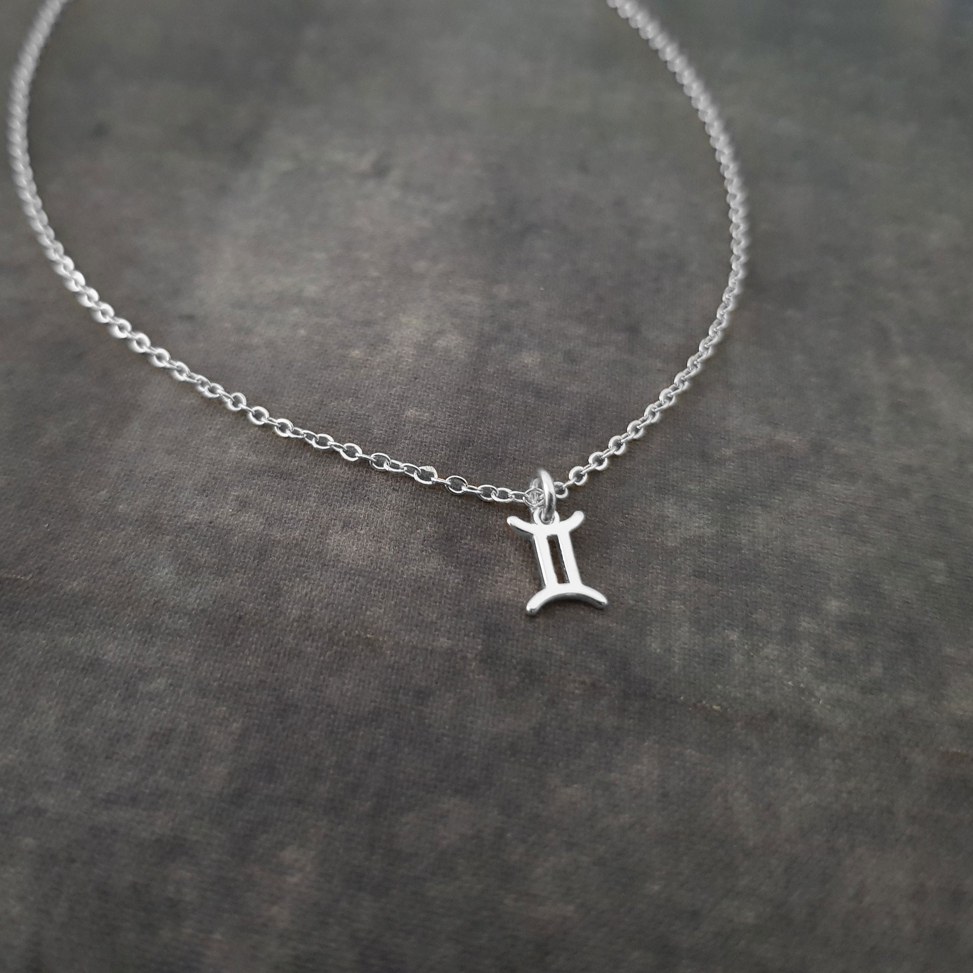 a silver initial necklace on a black surface