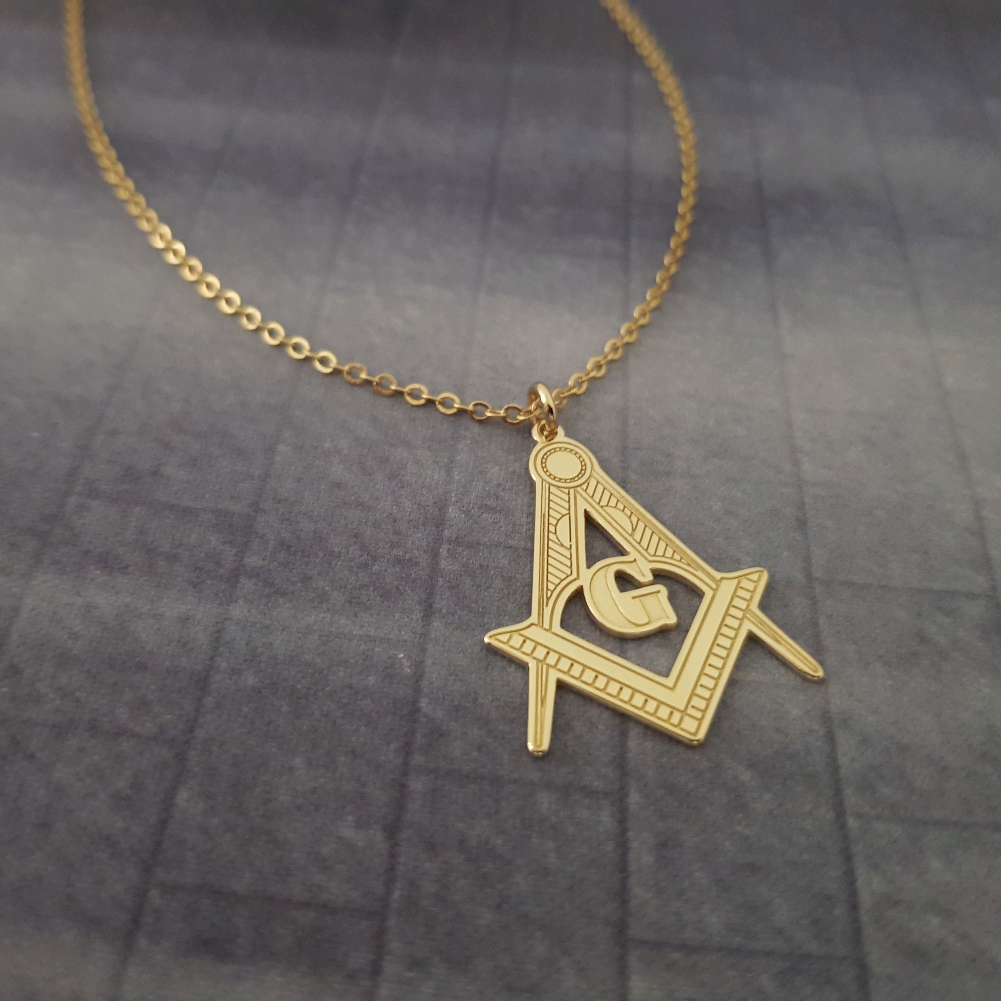 a gold necklace with a masonic symbol on it