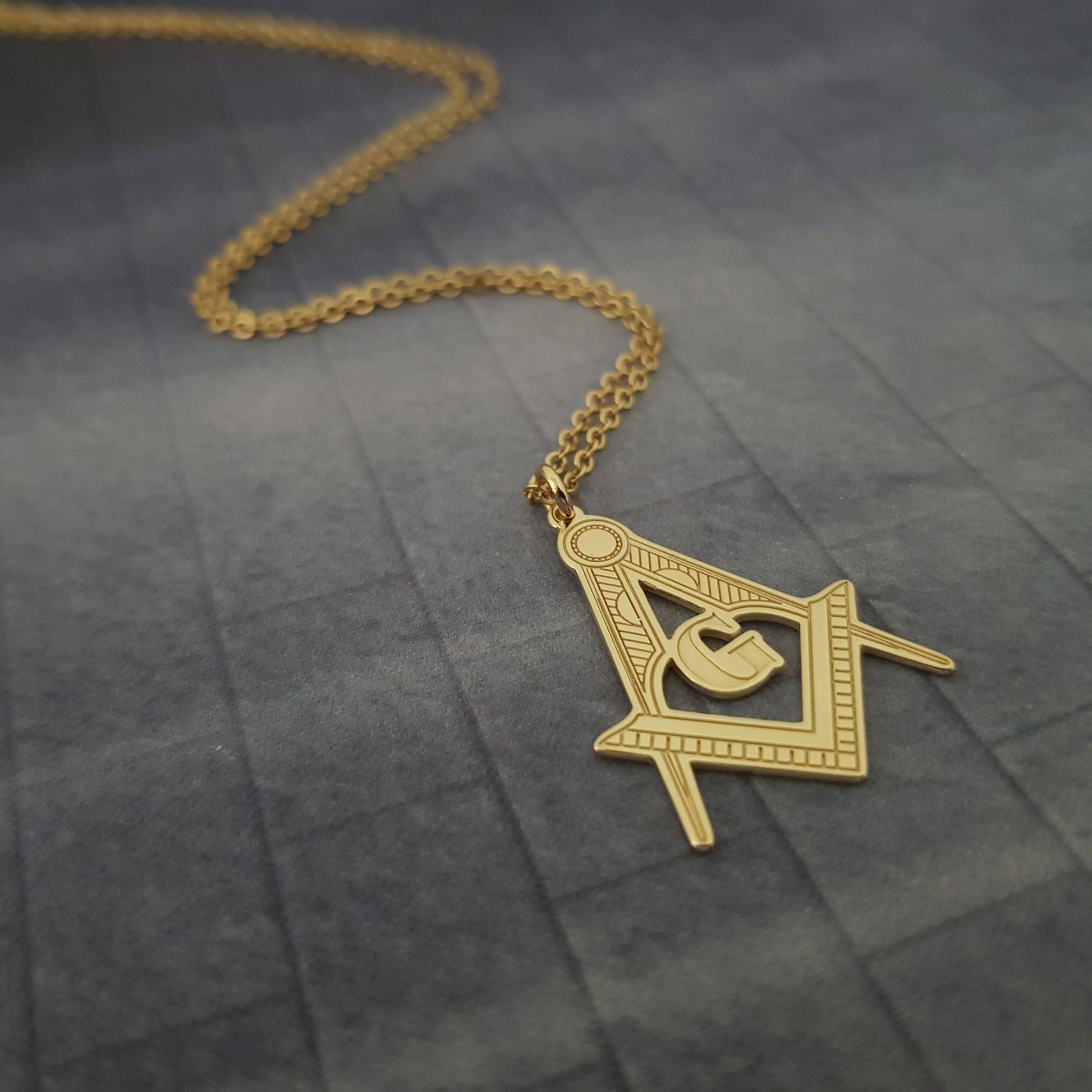 a gold necklace with a masonic symbol on it