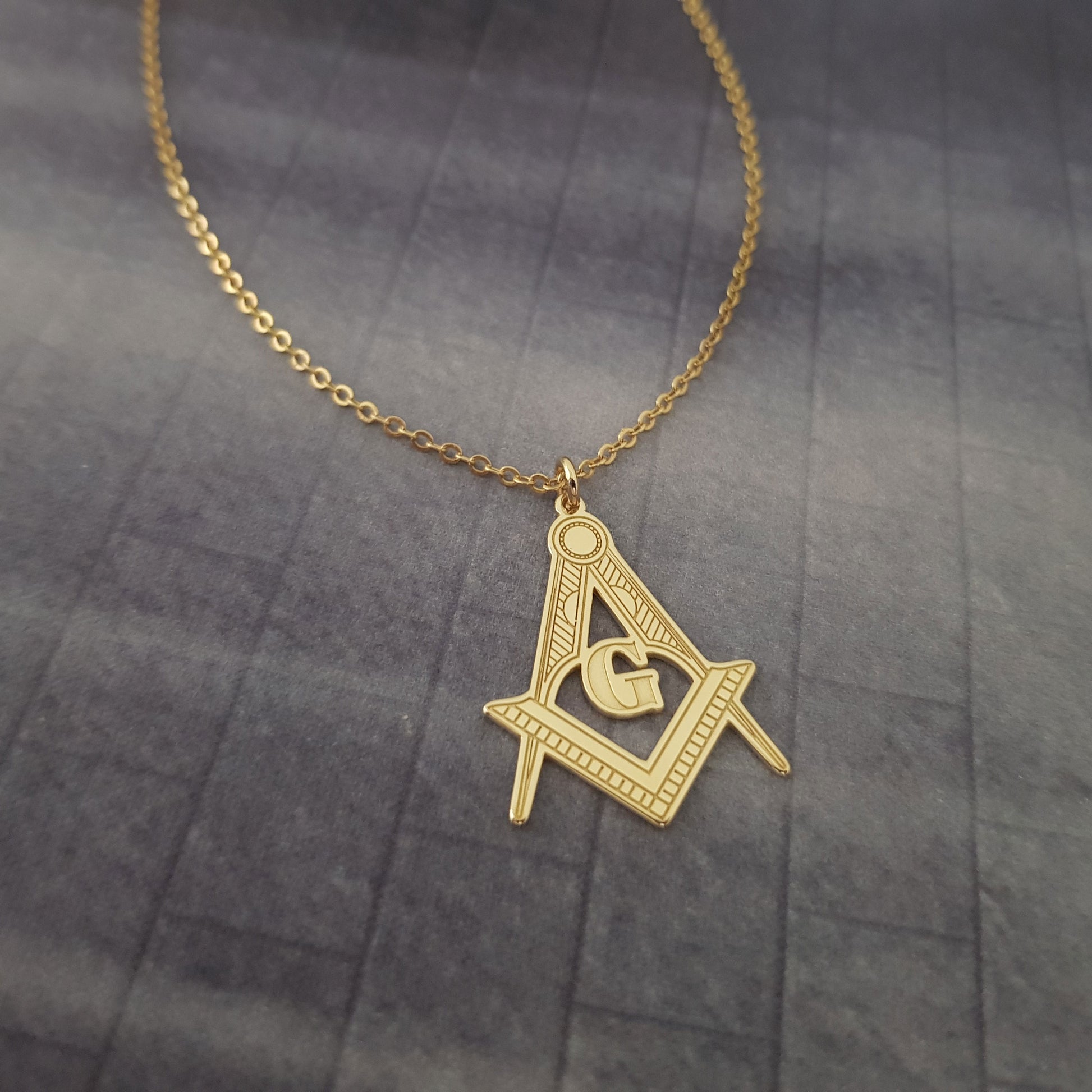 a gold necklace with a masonic symbol on it